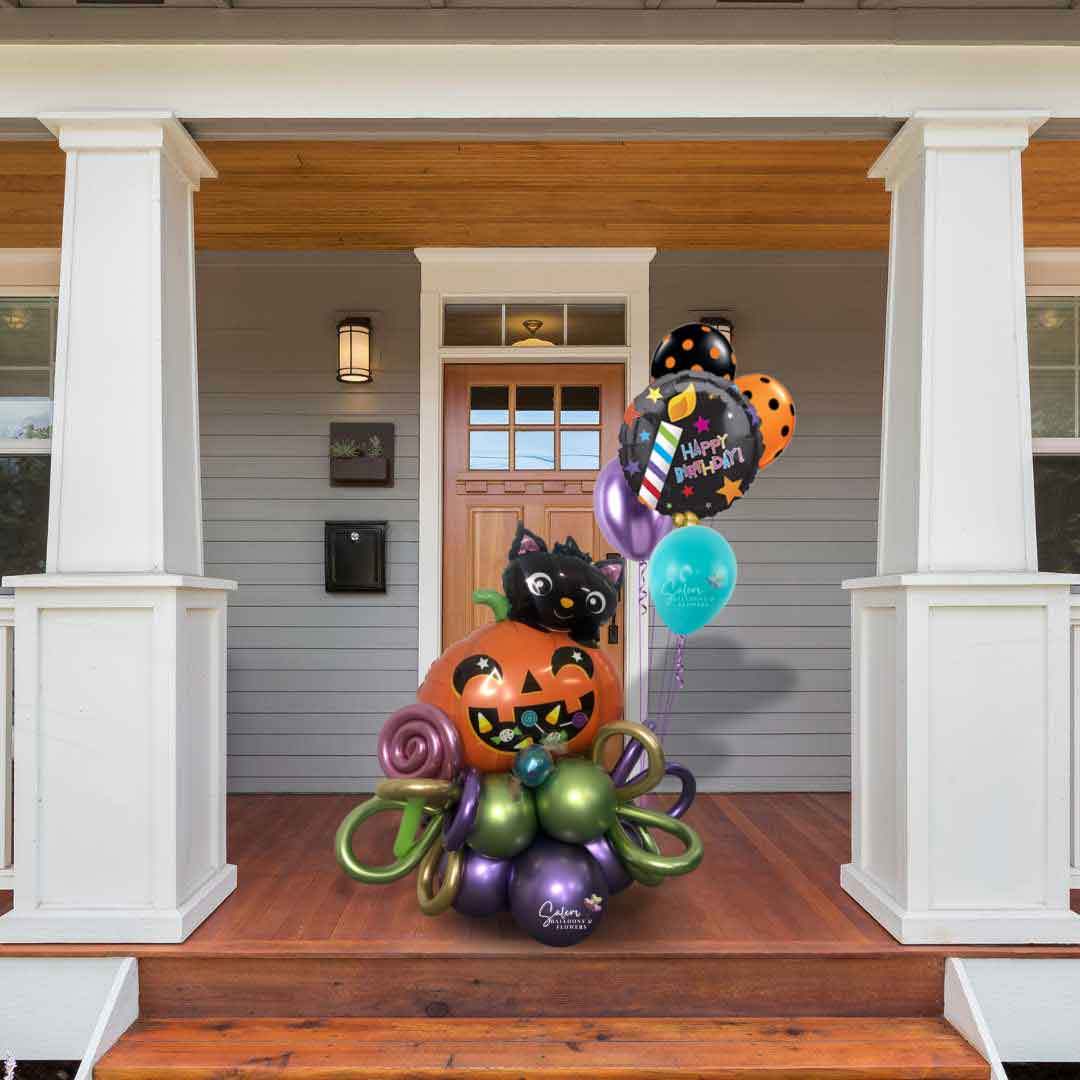 A Halloween themed balloon bouquet, featuring a pumpkin balloon with a cute black cat, decorated with helium balloons and curly balloons standing on a front porch.  Oregon Balloon delivery.